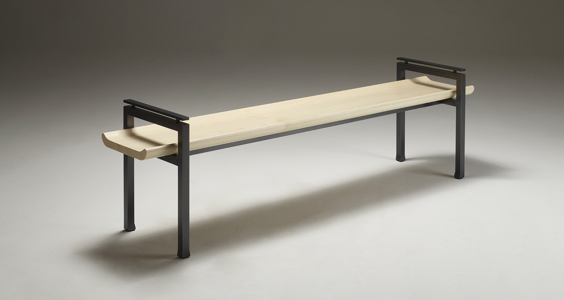 Panca passepartout dalle linee eleganti con struttura in bronzo e piano in diverse essenze lignee.