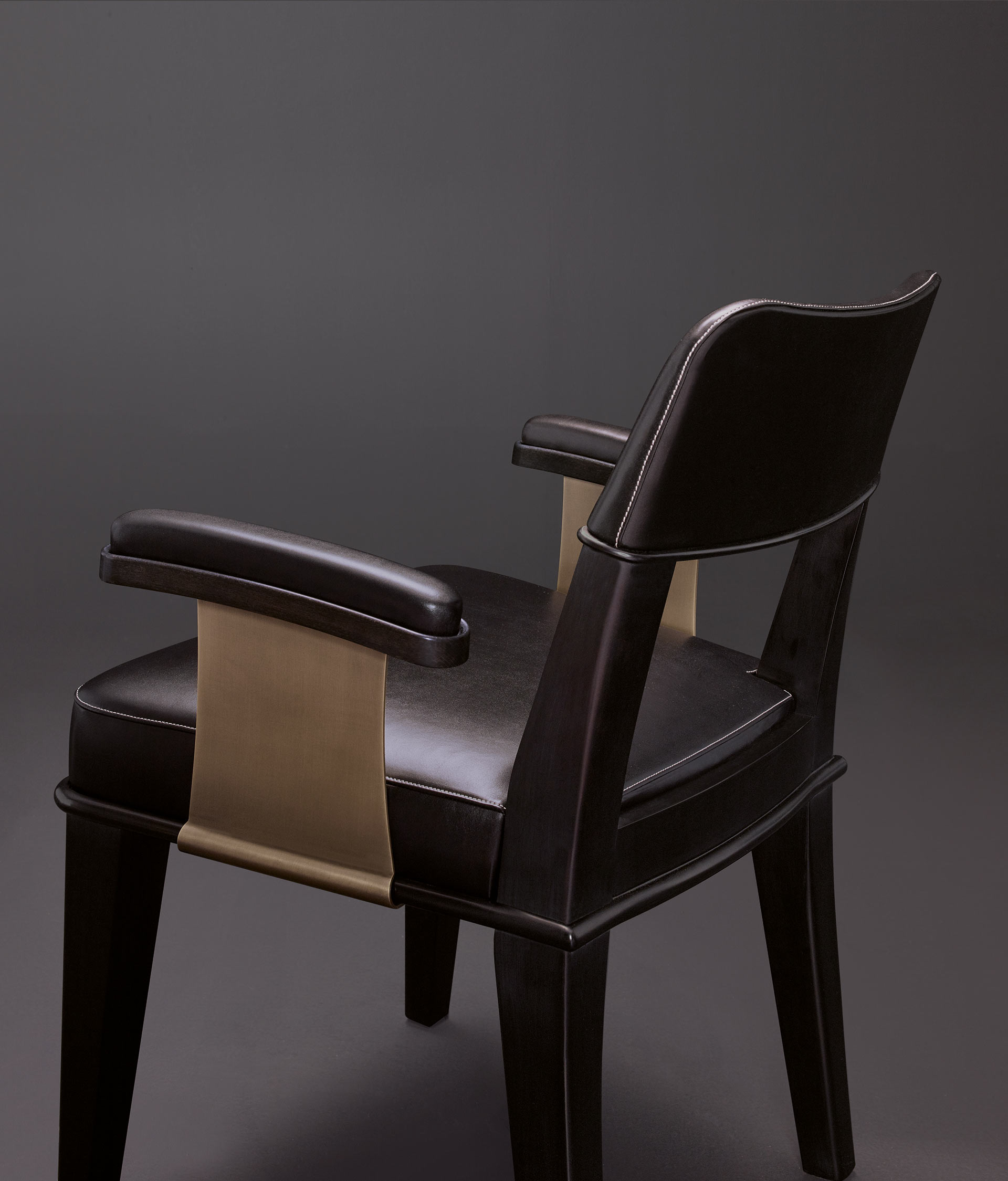 Detail of Vespertine, a wooden dining chair with leather seat and back and with armrests with bronze details, from Promemoria's Night Tales collection | Promemoria