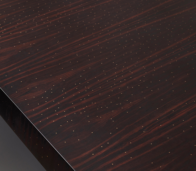 Top detail of Goffredo, a wooden dining table with a bronze base and checked or striped top, from Promemoria's catalogue | Promemoria